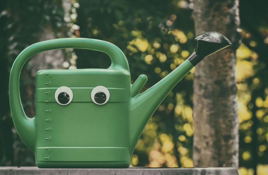 Googly-eyed watering can outdoors.
